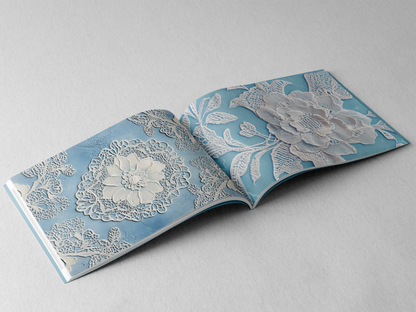 open book displaying the inner pages of a decorative paper prints pad showing blue doilie lace patterns